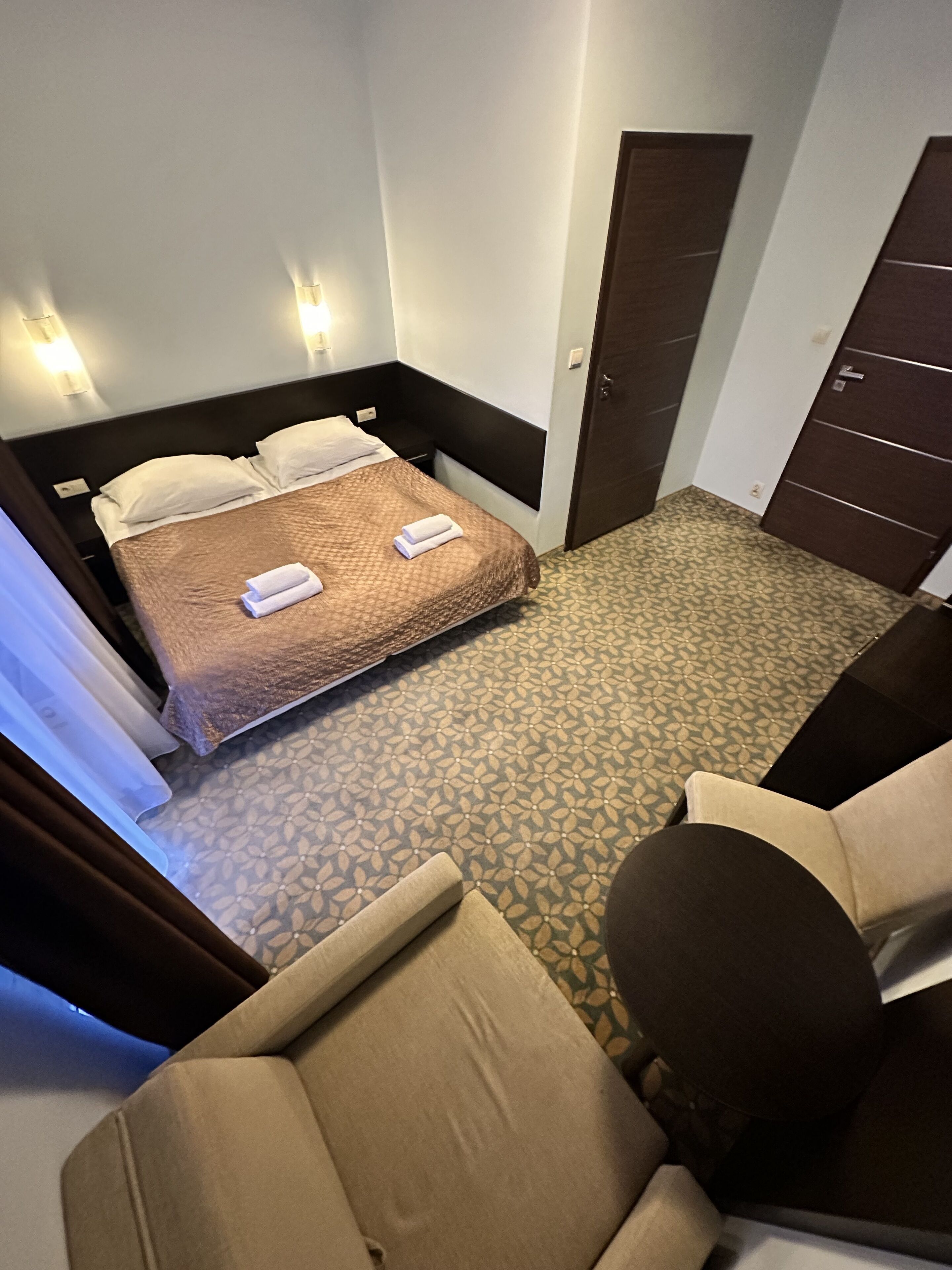 A hotel room with a bed, a chair, a desk, and a wardrobe.