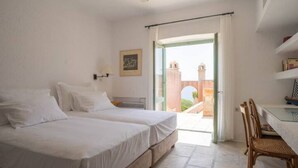 A hotel room with two beds, a dining table, and a view of a building through an open door. - Exquisite beachfront mansion, 5 bedrooms-Syros (Syros, Kyklades)