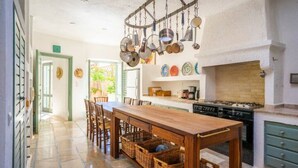 A kitchen with a wooden table, chairs, hanging pots, and a brick fireplace. - Exquisite beachfront mansion, 5 bedrooms-Syros (Syros, Kyklades)