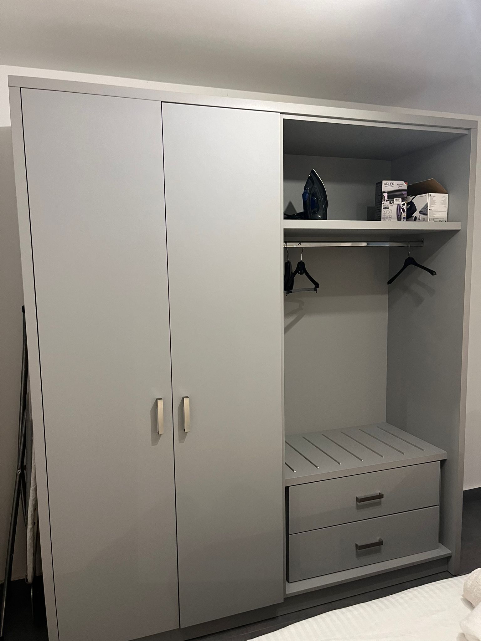 A grey wardrobe with two doors, a shelf, and a hanging space.