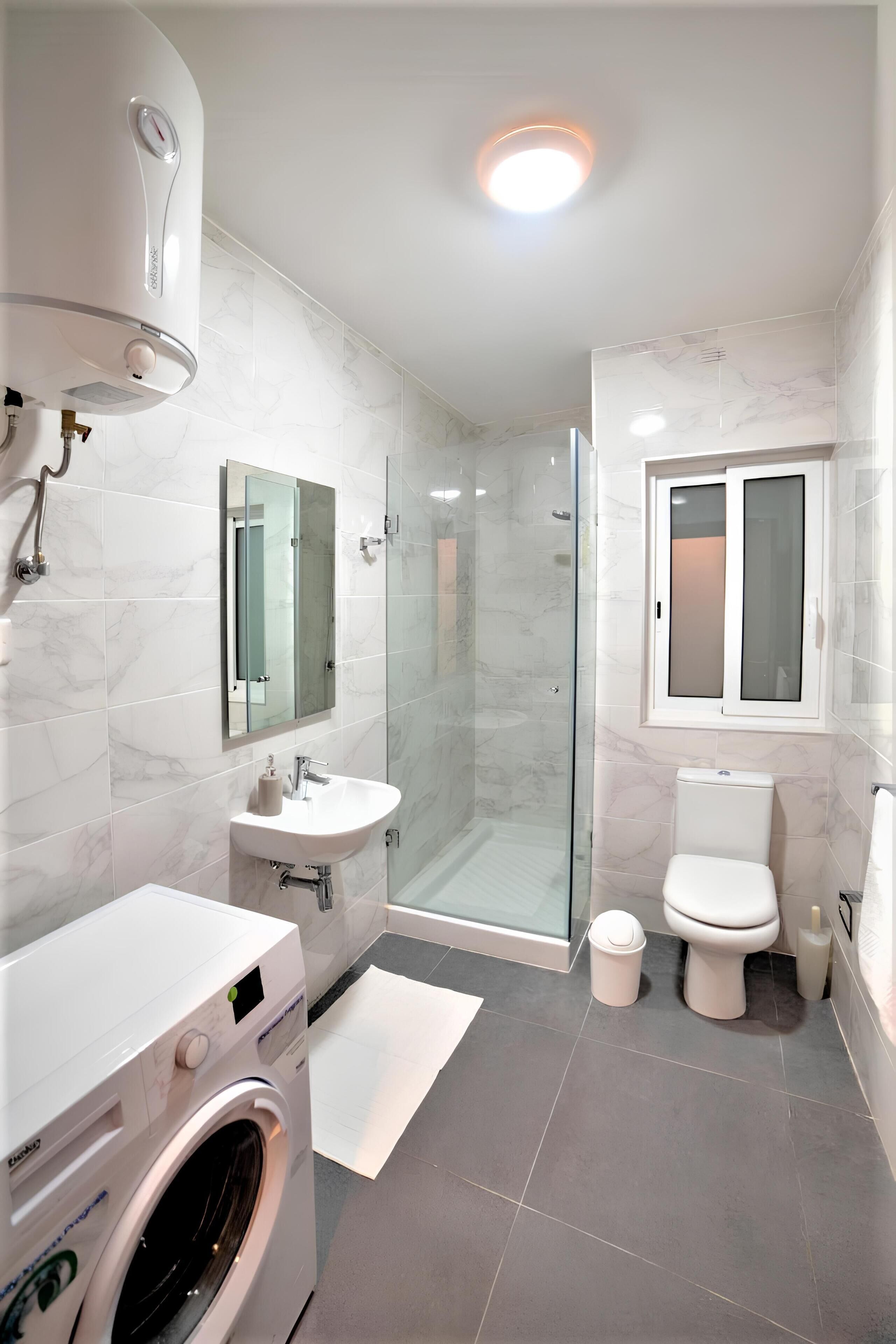 A modern bathroom with a glass-enclosed shower, a built-in sink, a toilet, and a washing machine.