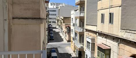 Ένας στενός δρόμος, με ψηλά κτίρια και στις δύο πλευρές του, τα οποία διαθέτουν μπαλκόνια, ένας καθαρός γαλάζιος ουρανός και σταθμευμένα αυτοκίνητα.