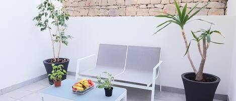 En balkon med en hvid stol, et lille bord med frugt og to plantekasser.