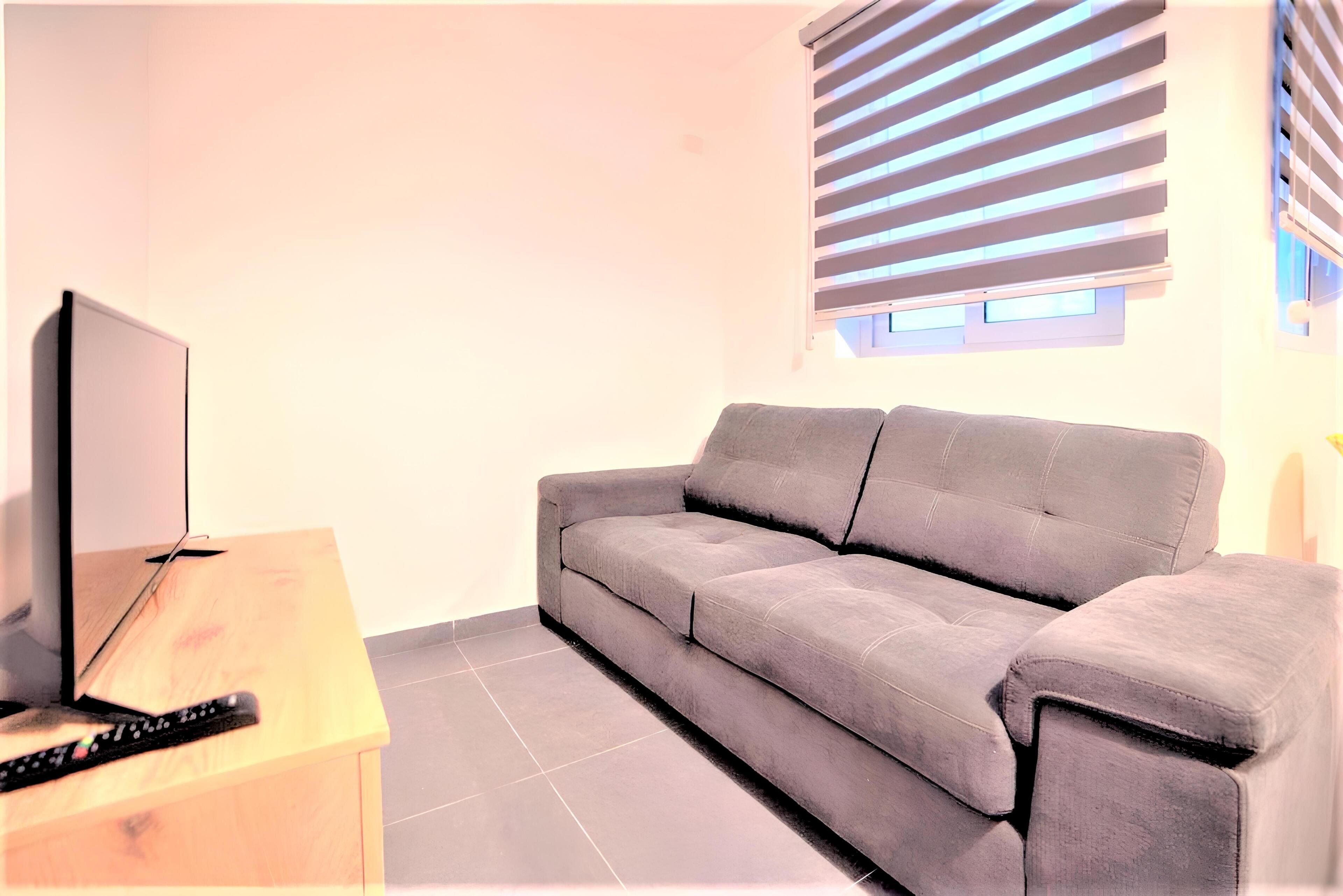 Un salón con un sofá gris, una mesita de madera y un televisor.