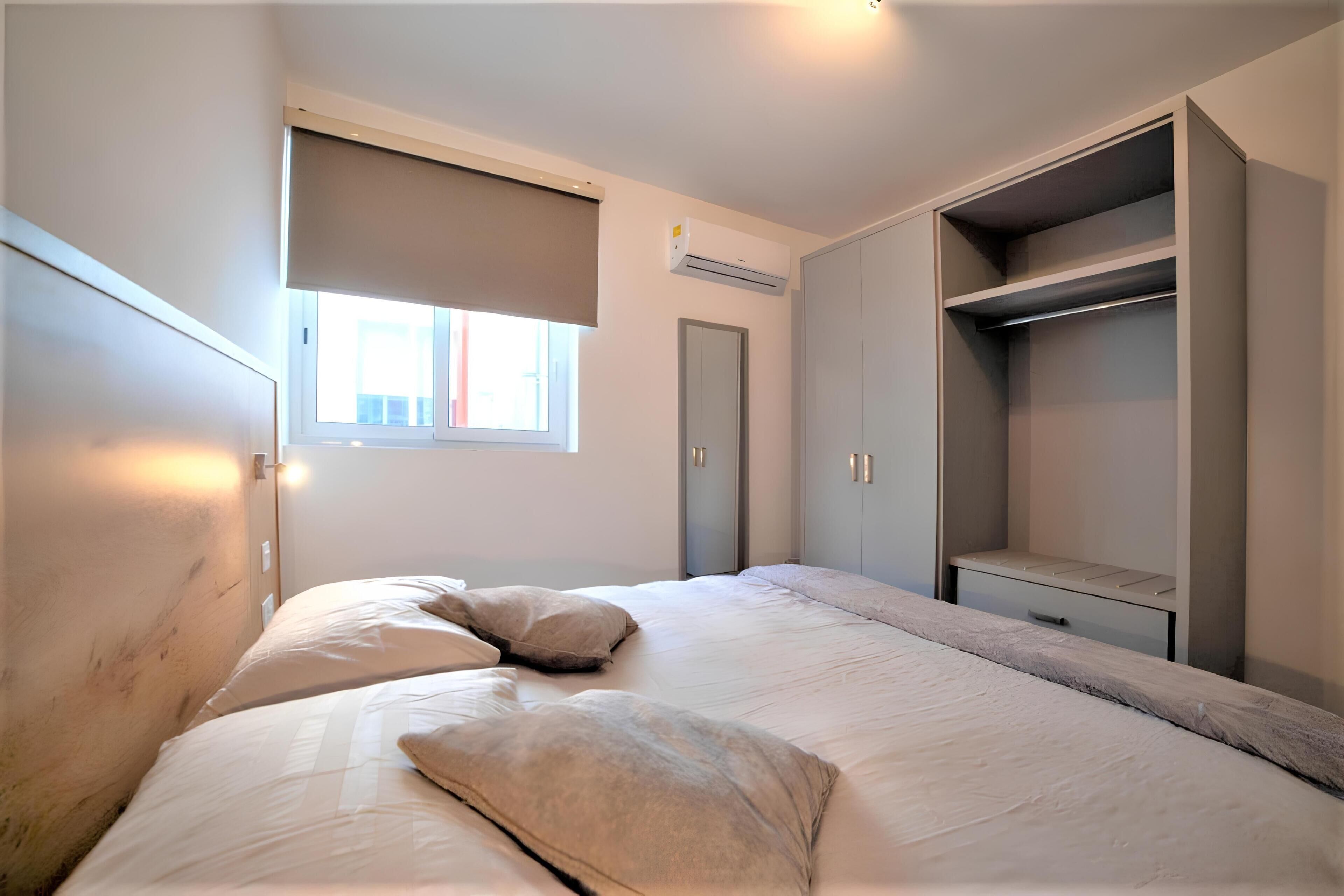 Un dormitorio con cama, almohadas, un armario y una ventana.