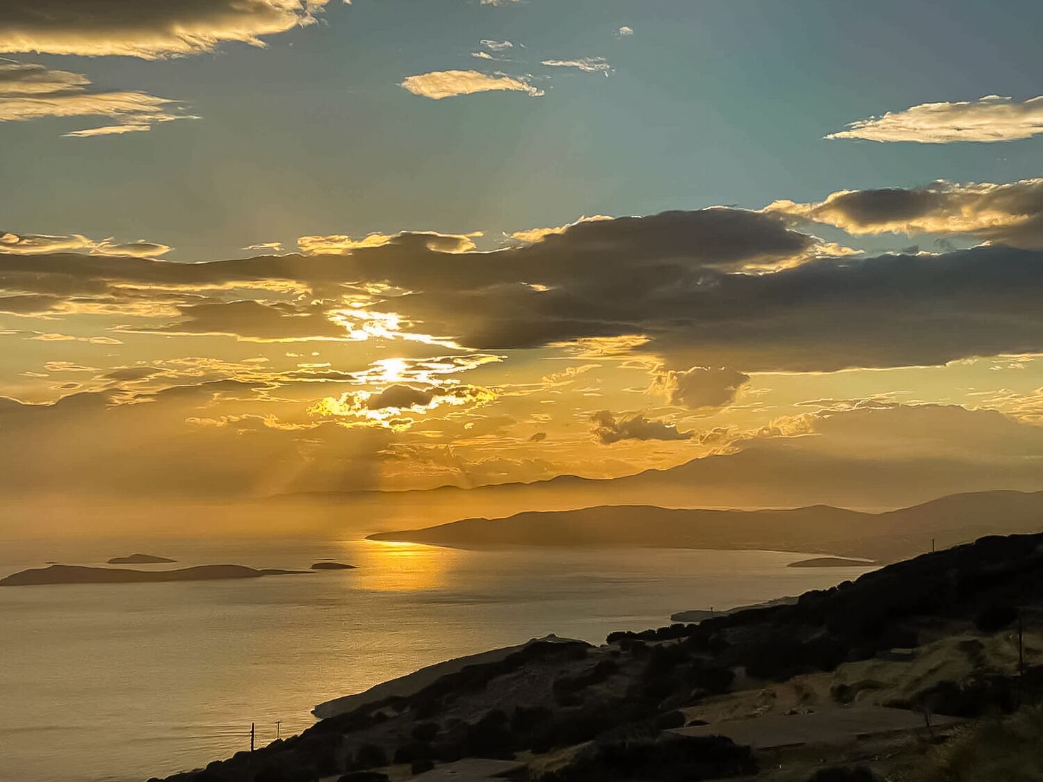 Un paysage côtier avec un coucher de soleil sur la mer, un terrain rocheux et des îles au loin.