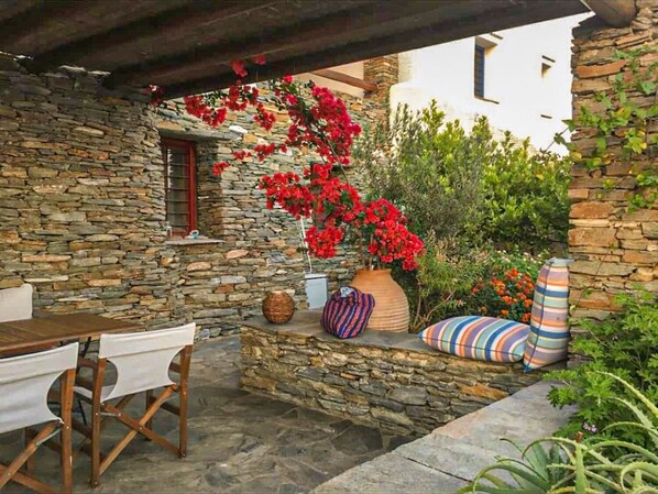 A stone patio with a table and chairs, a stone wall, and a variety of plants and flowers.