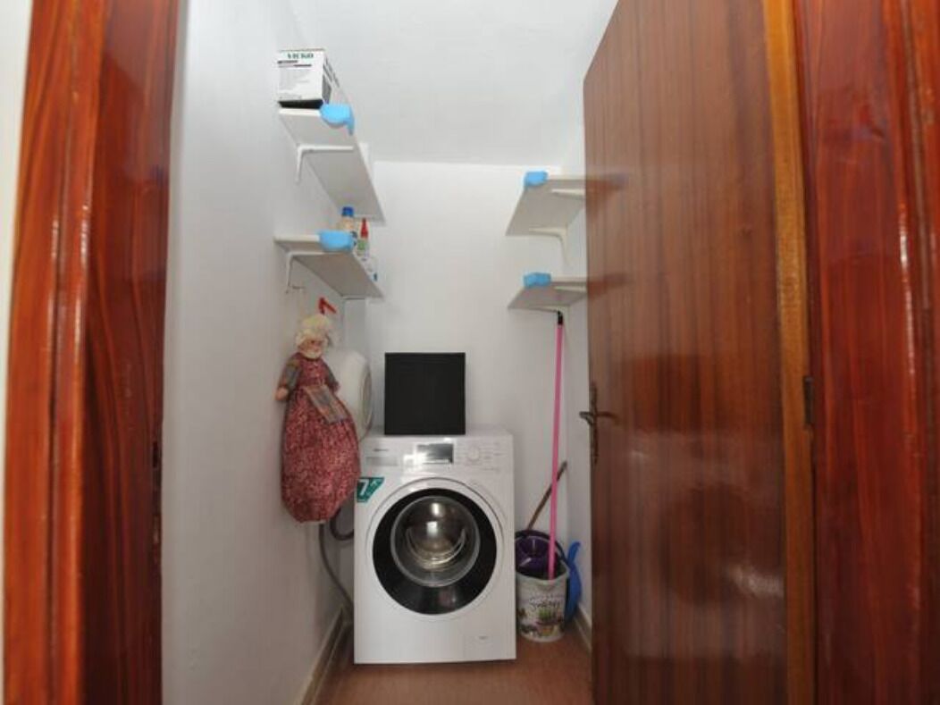 Uma lavanderia compacta com máquina de lavar, varal e prateleira pequena com produtos de limpeza.