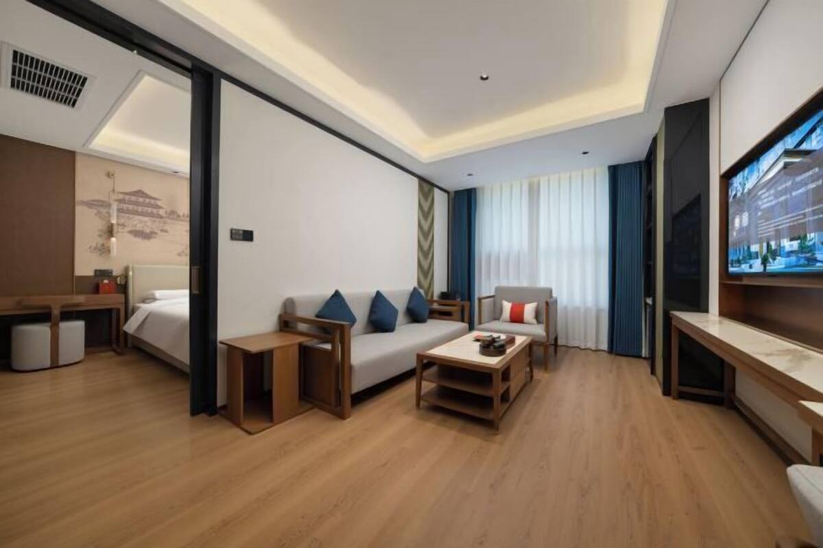 A modern hotel room with a wooden floor, a sofa, a small table, a bed, a desk, and a TV.