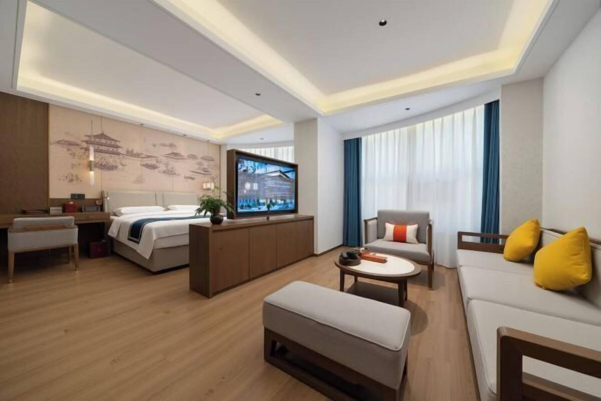 A modern hotel room with a bed, sofa, coffee table, and TV.