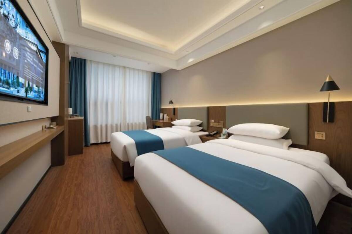 A hotel room with two beds, a TV, a desk, and a window with curtains.