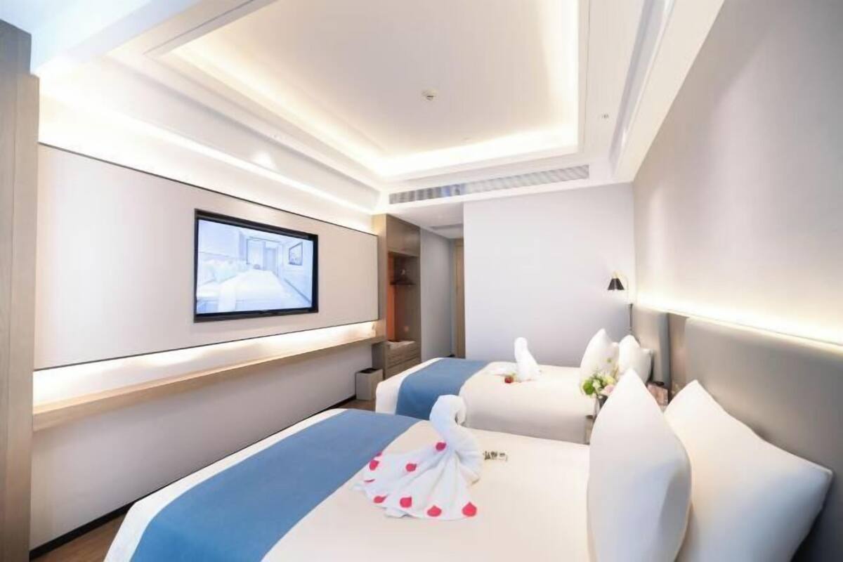 A modern hotel room with a large bed, a television mounted on the wall, and a separate seating area with a sofa and a small table.