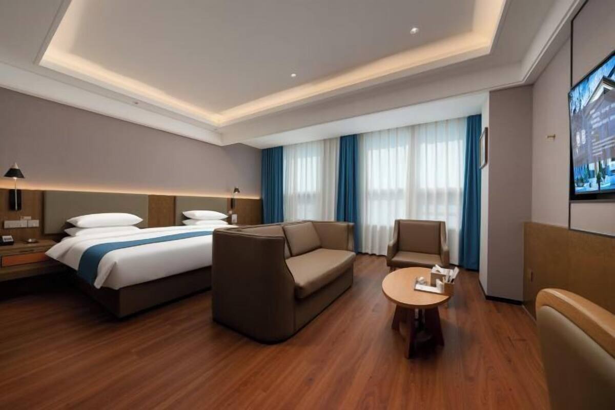 A hotel room with a bed, sofa, armchair, and a small table.