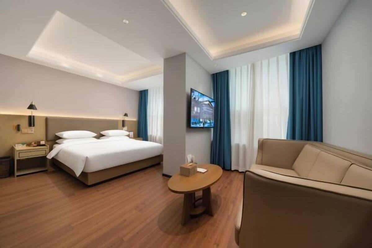A modern hotel room with a large bed, a sofa, a TV, and a small table.