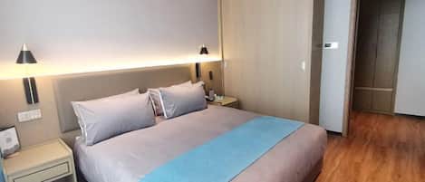 A hotel room with a large bed, two bedside lamps, a nightstand, and a wardrobe.
