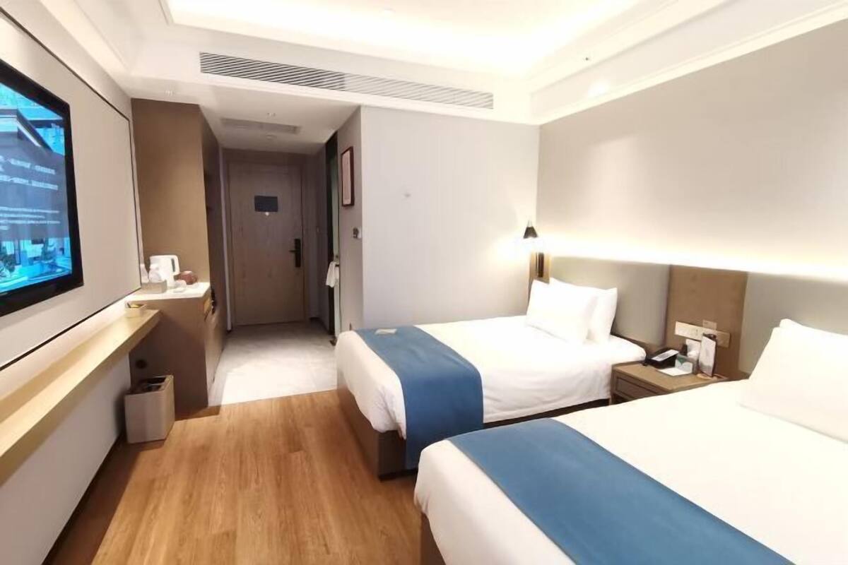 A hotel room with two beds, a TV, a desk, and a waste bin.