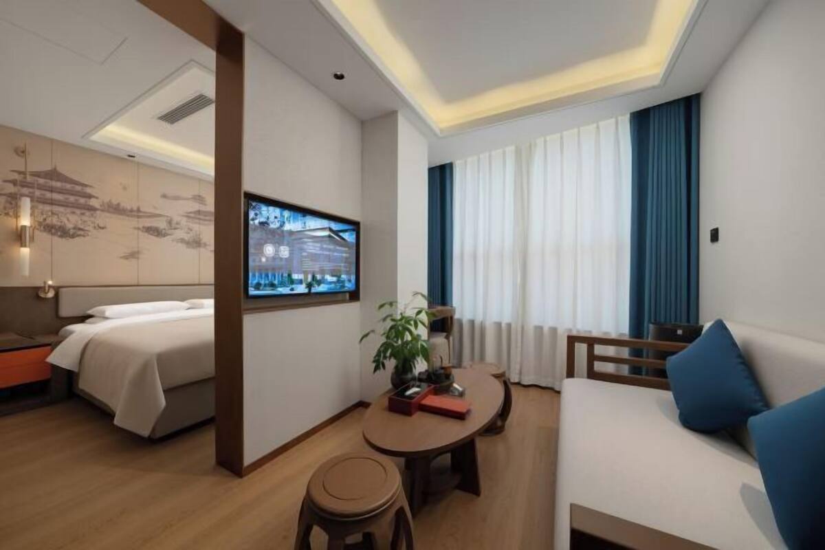A modern hotel room with a bed, a sofa, a dining table, and a TV.
