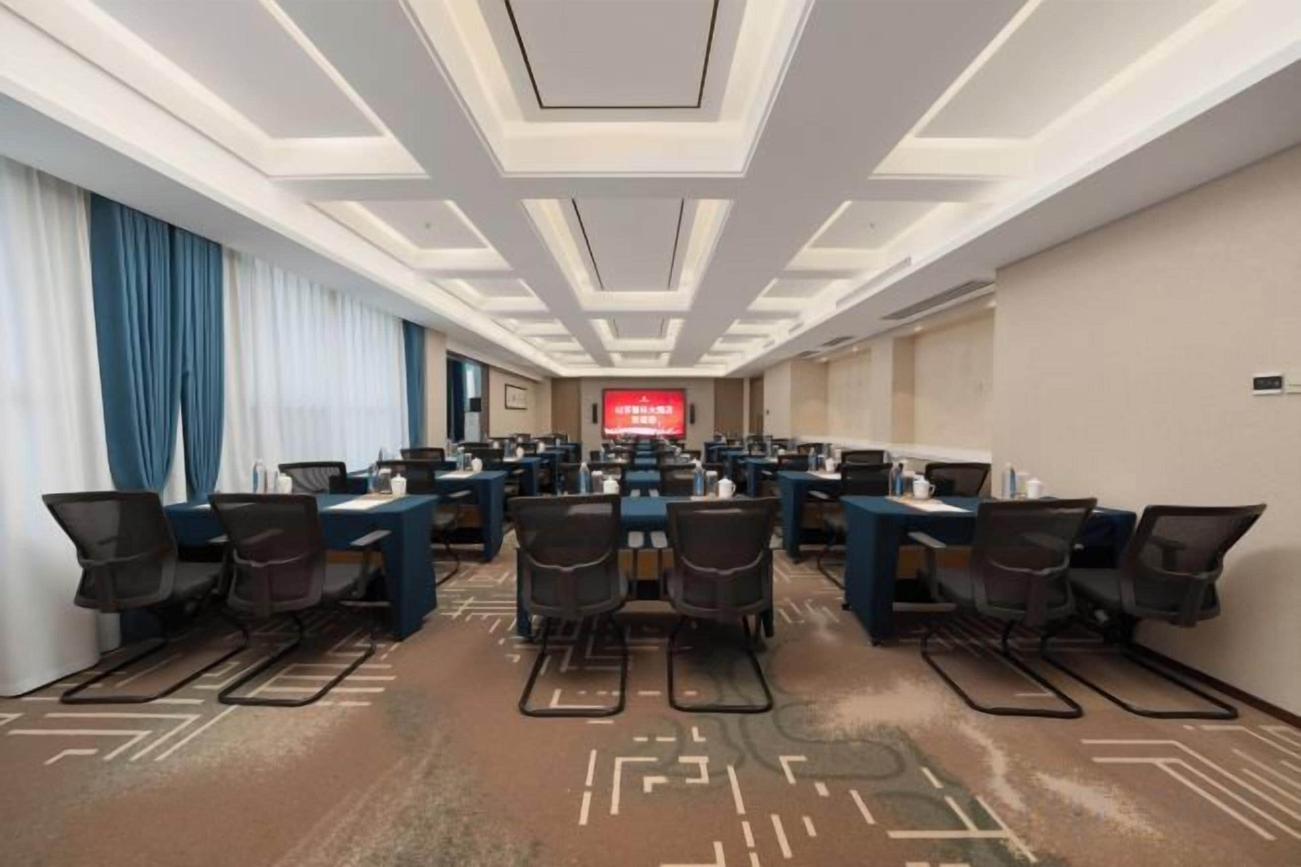 A conference room with multiple tables and chairs, a large screen at the front, and a patterned carpet.