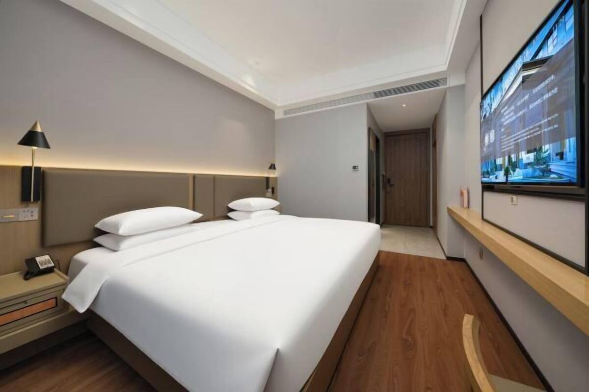A hotel room with a large bed, bedside tables, a lamp, a TV, and a wooden floor.