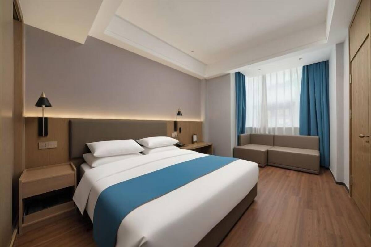 A modern hotel room with a large bed, bedside tables, a sofa, and a wardrobe.
