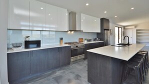 A modern kitchen with dark cabinetry, a central island, and a stainless steel range hood. - Off The Hook Kalbarri  (Kalbarri)