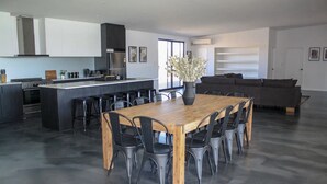 A modern kitchen with a central island, a dining area with a wooden table and chairs, and a grey sofa in a living area. - Off The Hook Kalbarri  (Kalbarri)