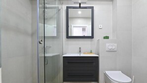 A modern bathroom with a glass shower enclosure, a dark vanity with a mirror, and a white toilet.