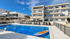 A modern hotel with a swimming pool, sun loungers, and a boat.