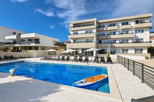 Un hôtel moderne doté d’une piscine, de chaises longues et d’un bateau.