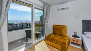 A modern hotel room with a large sliding glass door leading to a balcony with a city view.