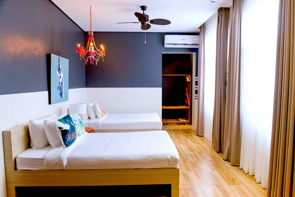 Une chambre dâhĂŽtel avec deux lits, un lustre, un ventilateur de plafond, un appareil de climatisation et une vue sur lâextĂ©rieur.