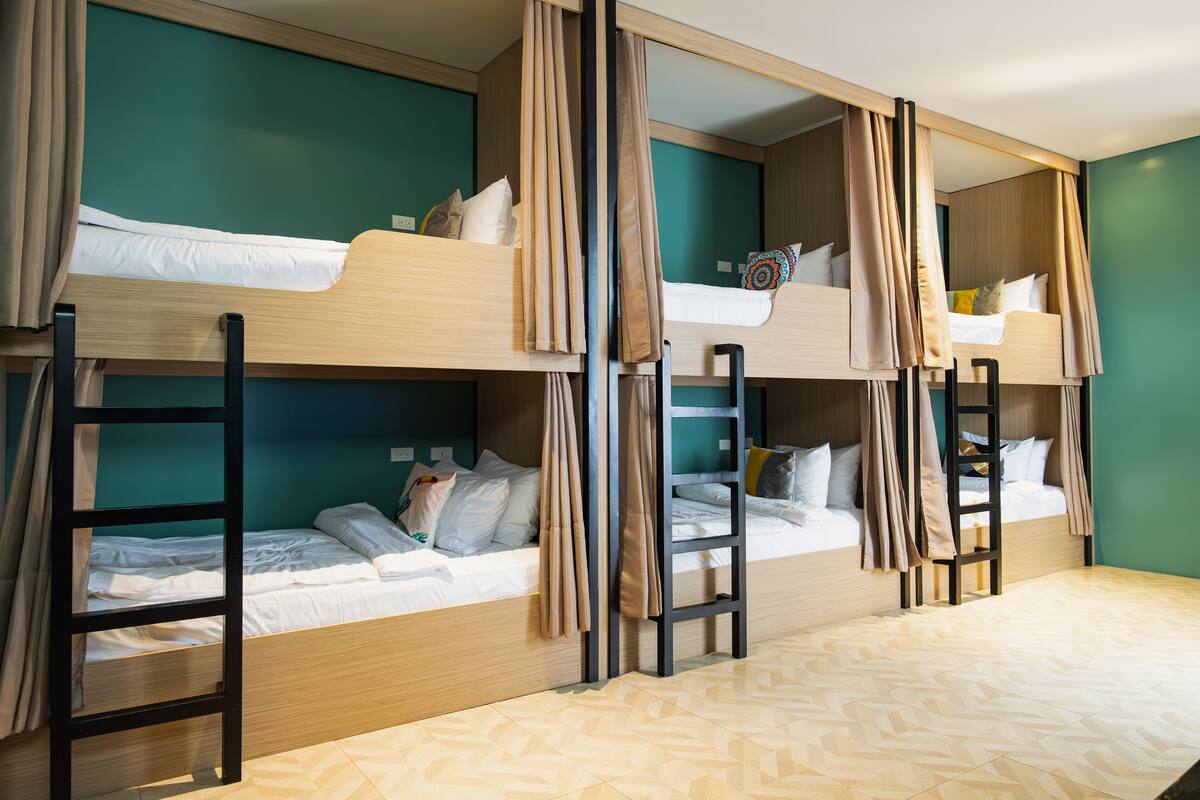 A dormitory-style room with bunk beds, wooden ladders, and teal walls.