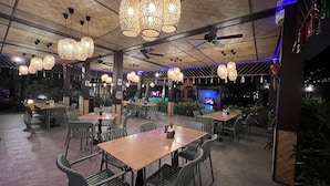 Un espacio interior para comer con varias mesas y sillas, ventiladores de techo e iluminación decorativa.