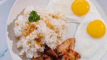 A plate with white rice, two sunny-side-up eggs, and grilled chicken, accompanied by a small bowl of watermelon.