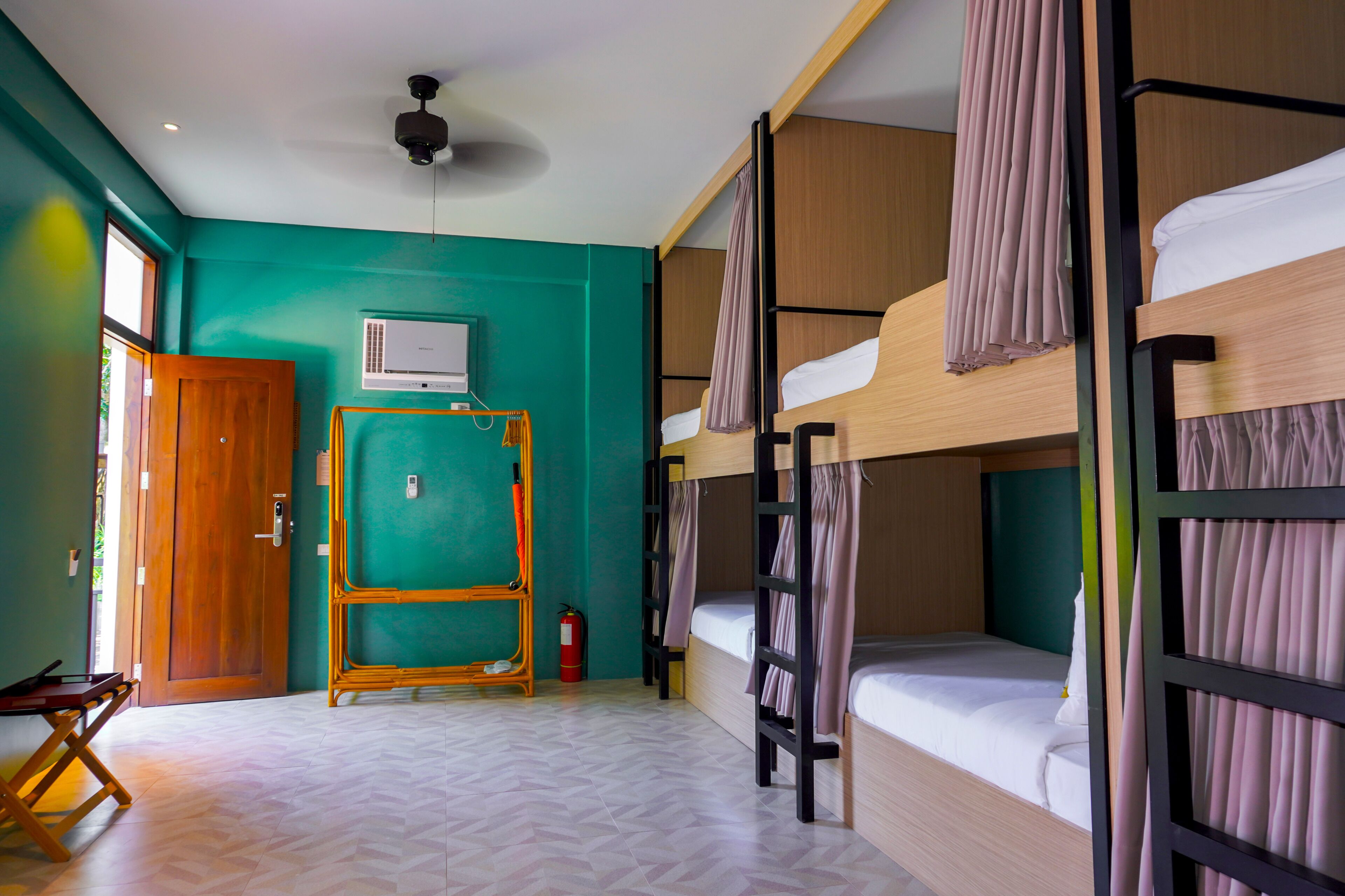 A room with bunk beds, a wooden door, a window, a ceiling fan, and a fire extinguisher.