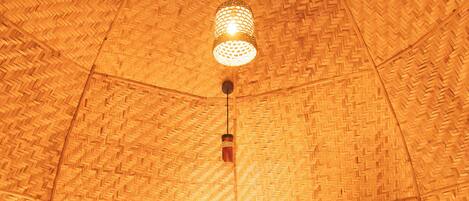 A room with a woven ceiling, a bed with white bedding, two bedside lamps, and a wall-mounted air conditioner.