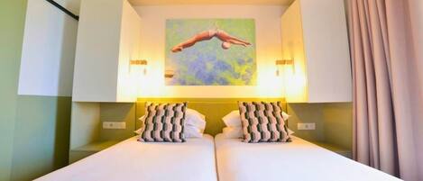 A hotel room with two beds, a painting of a diver, and a curtain on the right.