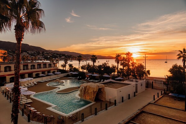 Un resort con piscina, sillas de descanso y vista al atardecer sobre el mar.
