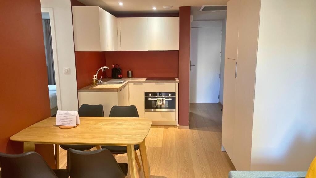 A compact kitchen with white cabinets, a sink, and an oven. There is a dining table with chairs and a menu on it.