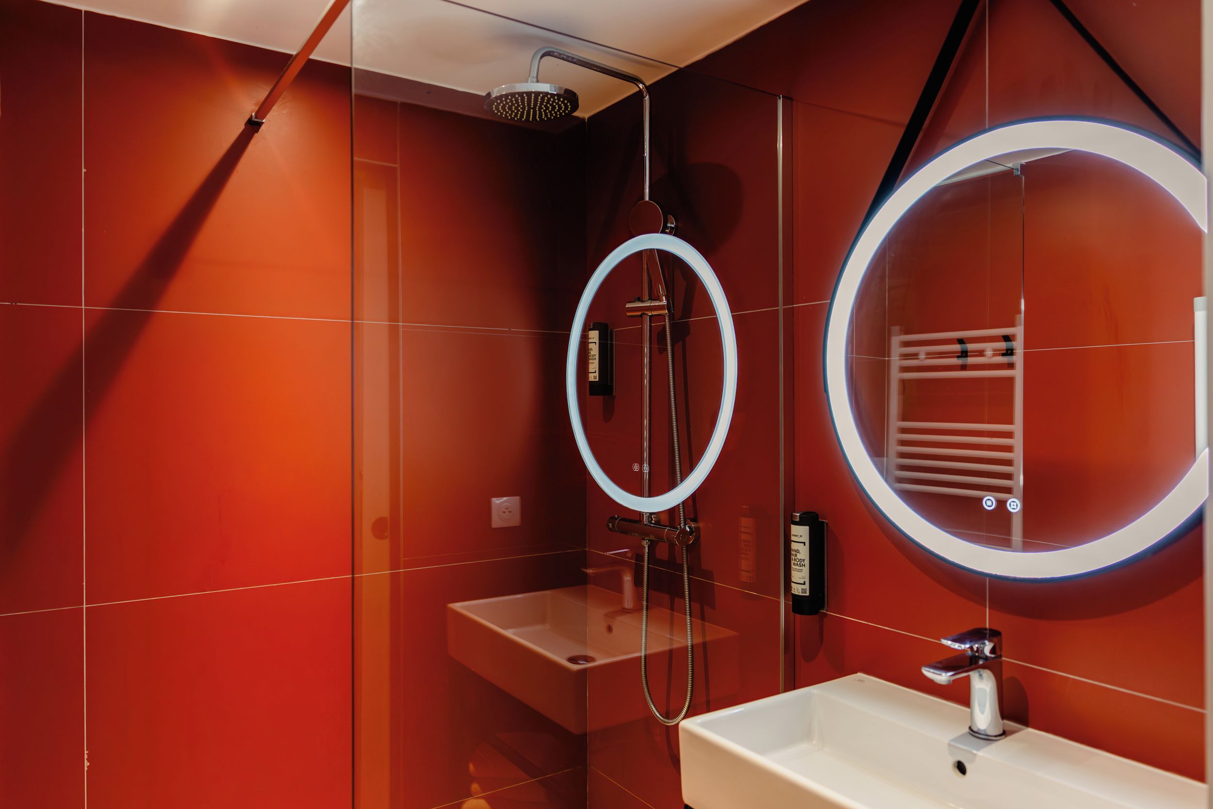 A modern bathroom with a glass-enclosed shower, a round mirror, and a white sink.