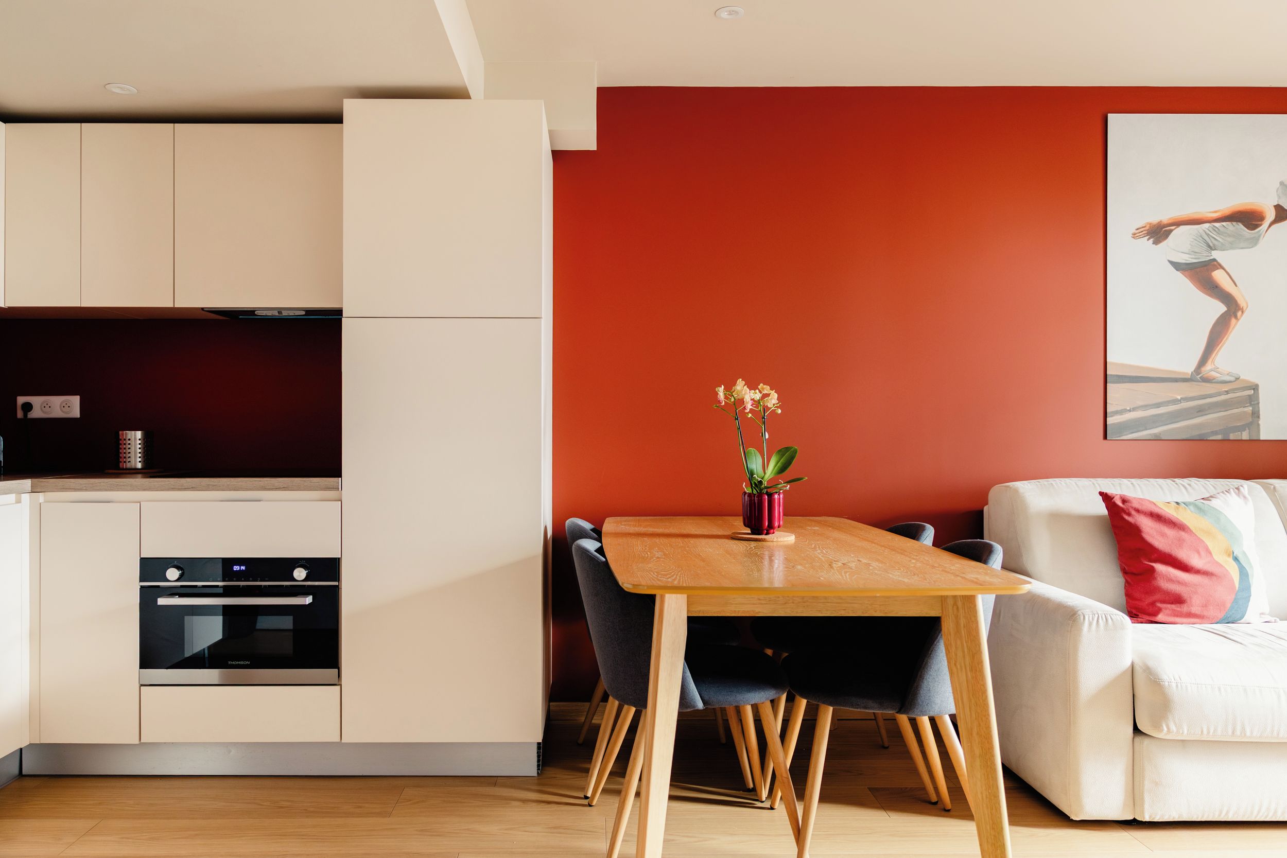 Een moderne keuken met een ingebouwde oven en een eethoek met een houten tafel en stoelen.