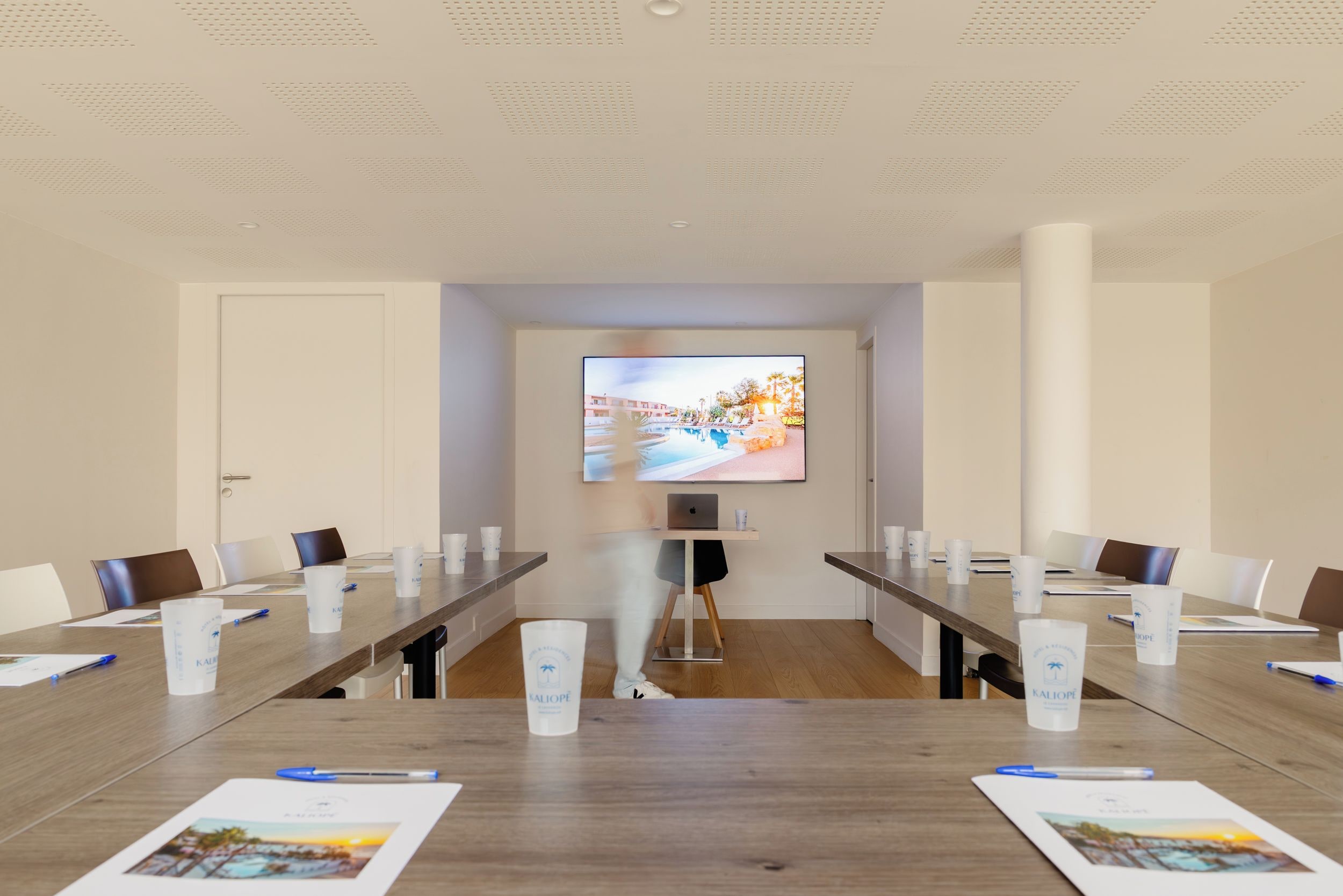 A conference room with a long table, chairs, a projector screen, and a laptop.