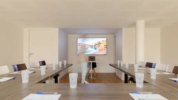 Ein Konferenzraum mit einem langen Tisch, Stühlen, einer Projektionsleinwand und einem Laptop.