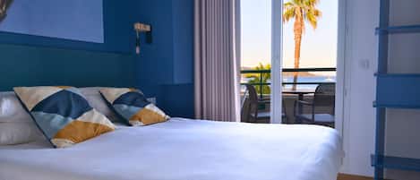 Habitación de hotel con una cama grande, vista al océano y un balcón con una palmera.