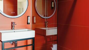 A modern bathroom with a glass-enclosed shower, a round mirror, and a white sink.