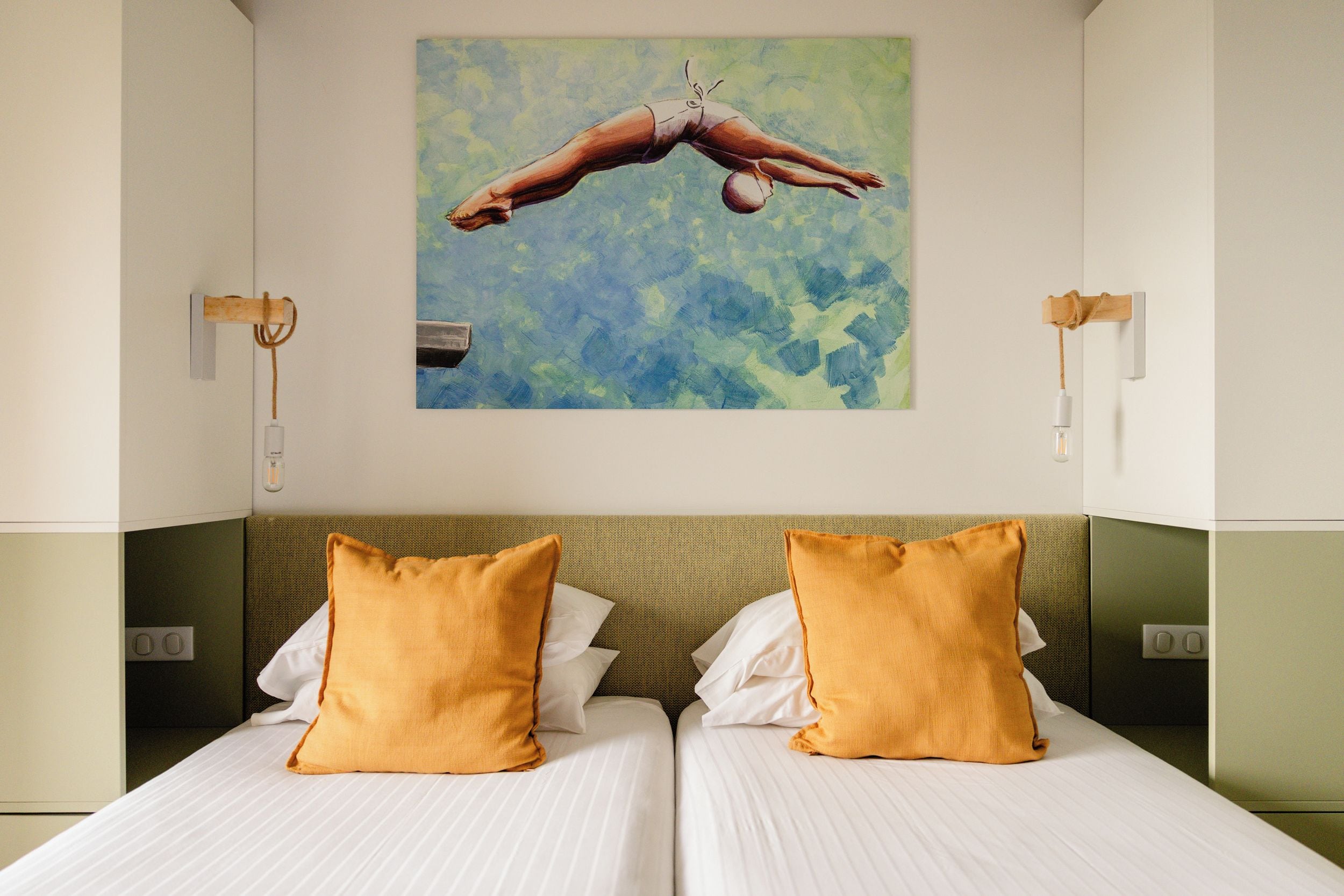 Ein Hotelzimmer mit einem Bett, zwei Kissen, einer Wandleuchte und einem Bild von einem Taucher.