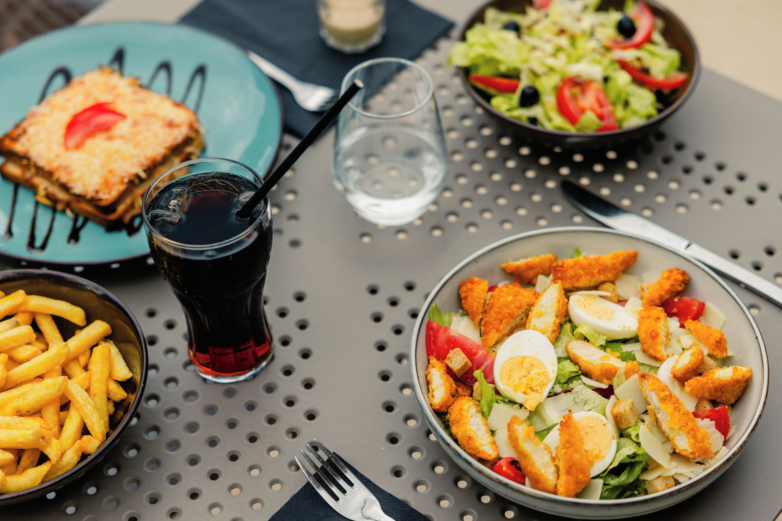 Une table dressée avec un repas composé d’une salade, de pain, de frites et d’une boisson.
