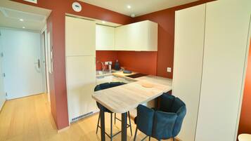 A compact kitchen with a wooden table and two blue chairs, a white refrigerator, and a white oven.