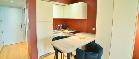 A compact kitchen with a wooden table and two blue chairs, a white refrigerator, and a white oven.