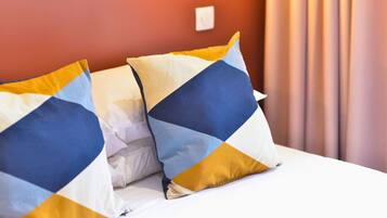 A bed with white bedding and two decorative pillows with geometric patterns.